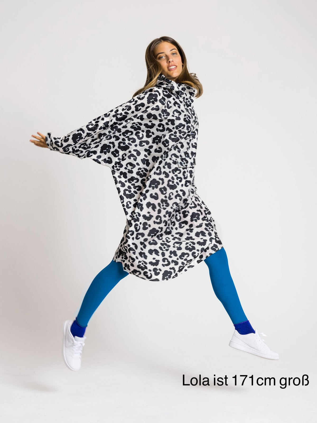 Ela Mo™ Regenponcho | Leo. Eine Frau mit Regenponcho, inklusive Produkt-Höhenangabe.