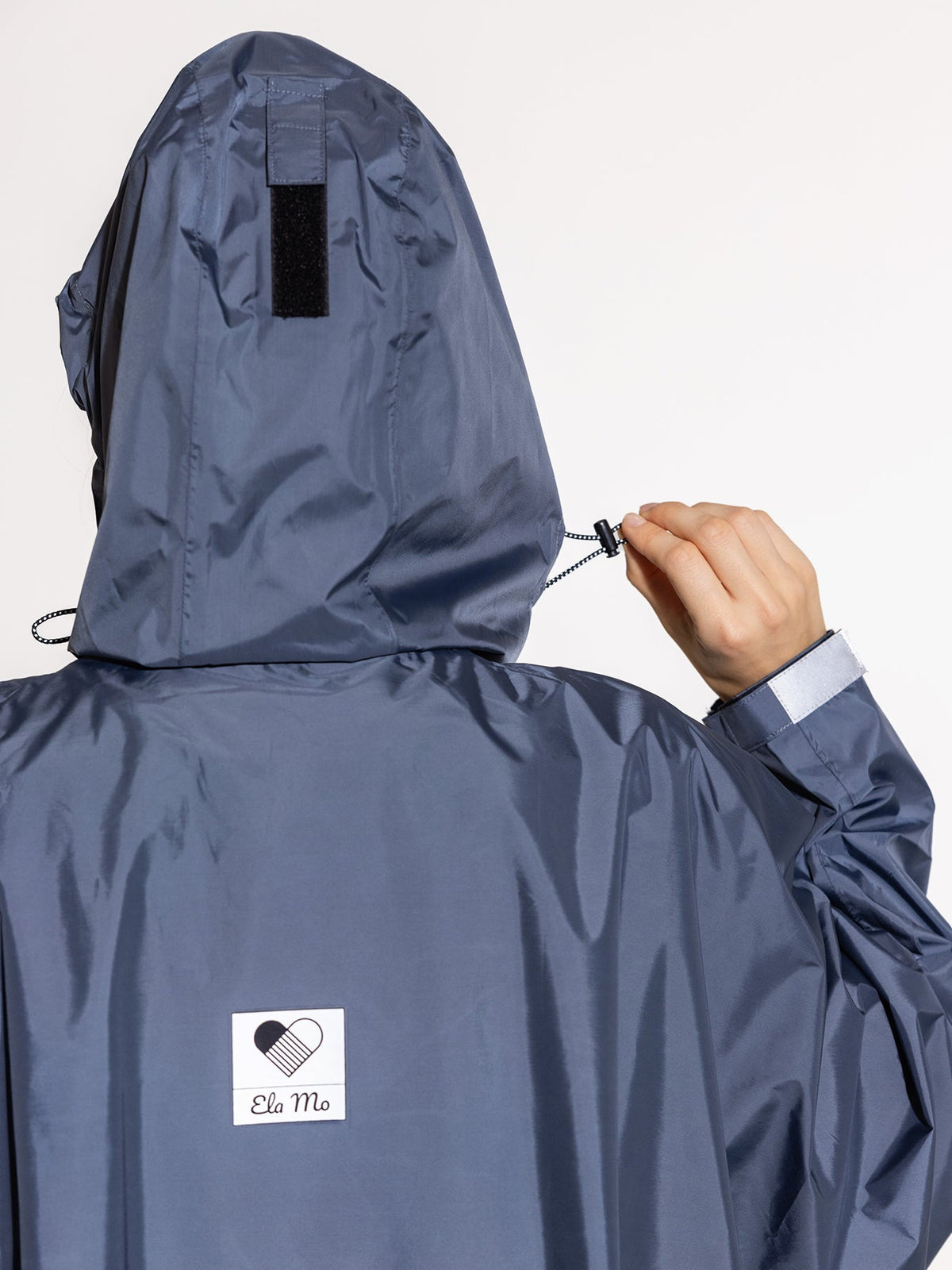 Ela Mo™ Regenponcho | Navy. Eine Frau im Regenponcho mit Kapuze, Ansicht von hinten.