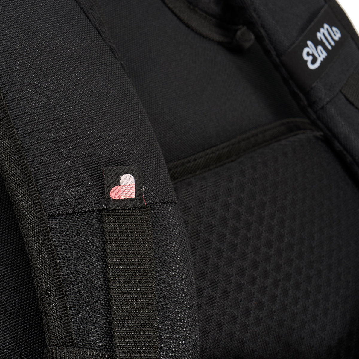 Ela Mo™ Everywhere Daypack | Embroidery Edition Upsy Daisy. Schulterriemen mit kleinem Herzchen und Herstellerlogo darauf.
