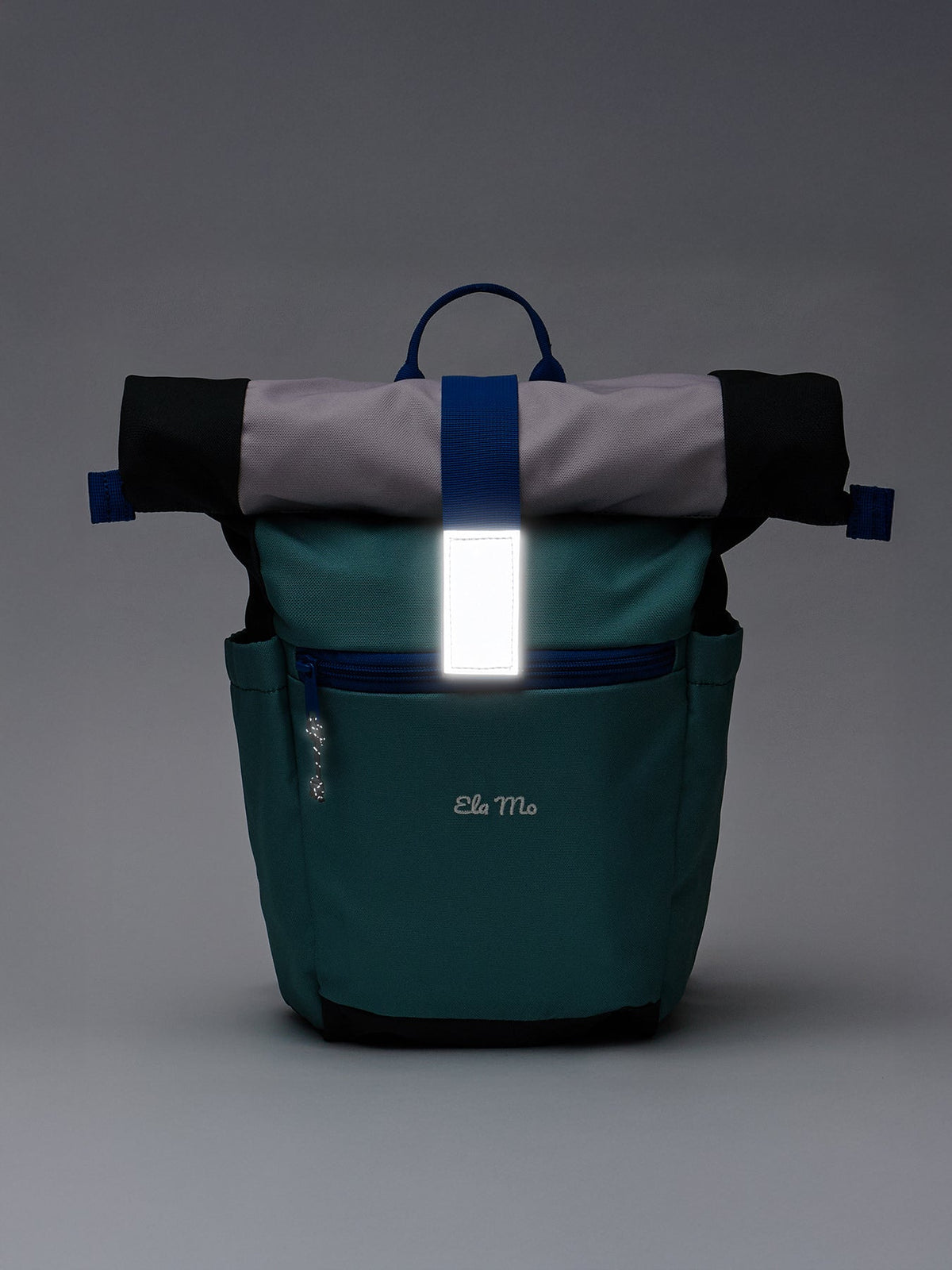 Ela Mo™ Kinderrucksack (6-10 Jahre) | Blue Mint. Ein blauer Rucksack im Dunkeln mit reflektierendem Verschluss.