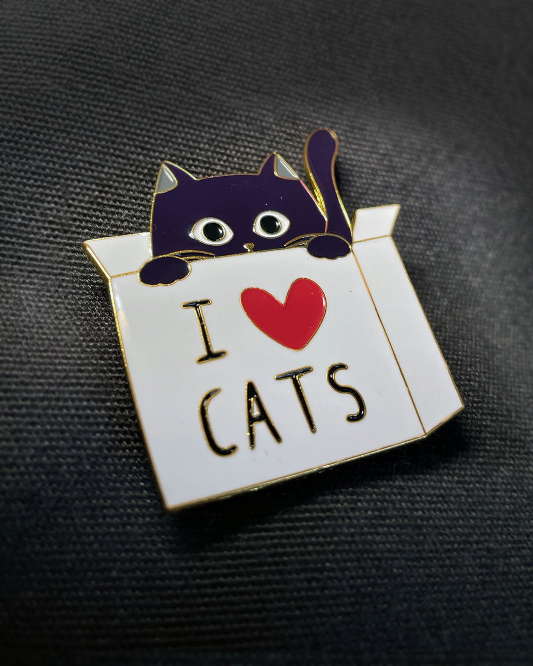 Ela Mo™ Pin für Rucksäcke | Cat. Nahansicht eines kleinen Pins, befestigt auf dem schwarzen Rucksack.