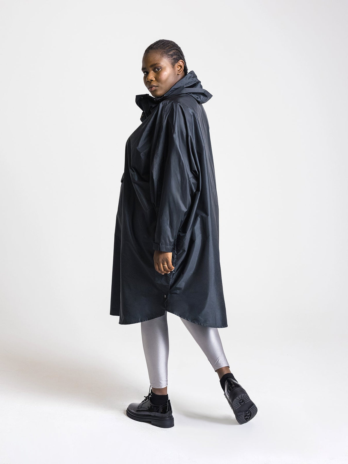 Ela Mo™ Regenponcho | Black. Frau mit Regenponcho von der linken Seite auf weißem Hintergrund.