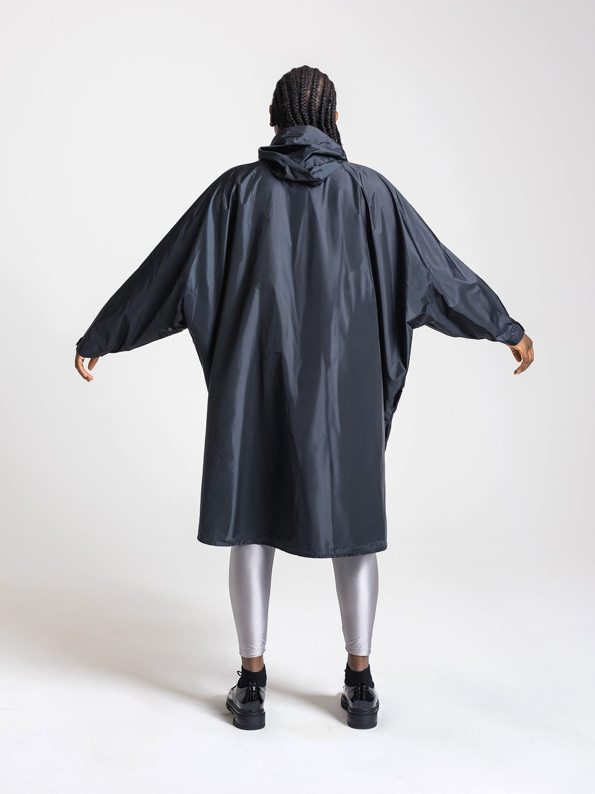 Ela Mo™ Regenponcho | Black. Frau mit Regenponcho von hinten auf weißem Hintergrund.