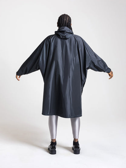Ela Mo™ Regenponcho | Black. Frau mit Regenponcho von hinten auf weißem Hintergrund.