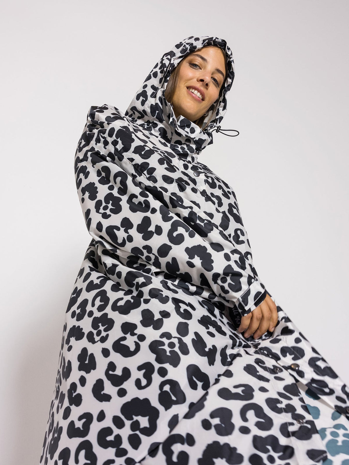 Ela Mo™ Regenponcho | Leo. Lachende Frau mit Regenponcho und Kapuze.