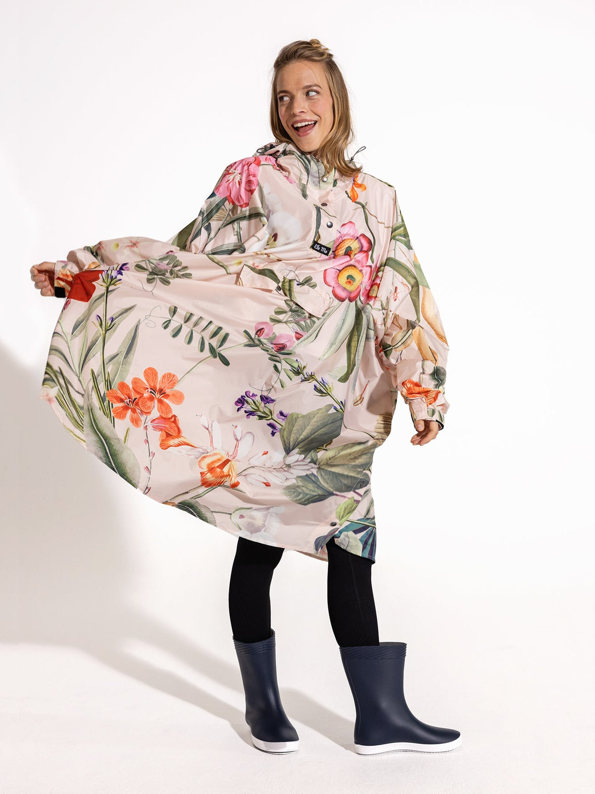 Ela Mo™ Regenponcho | Luxe. Eine Frau im Regenponcho, der ausreichend breit ist, auf weißem Hintergrund.