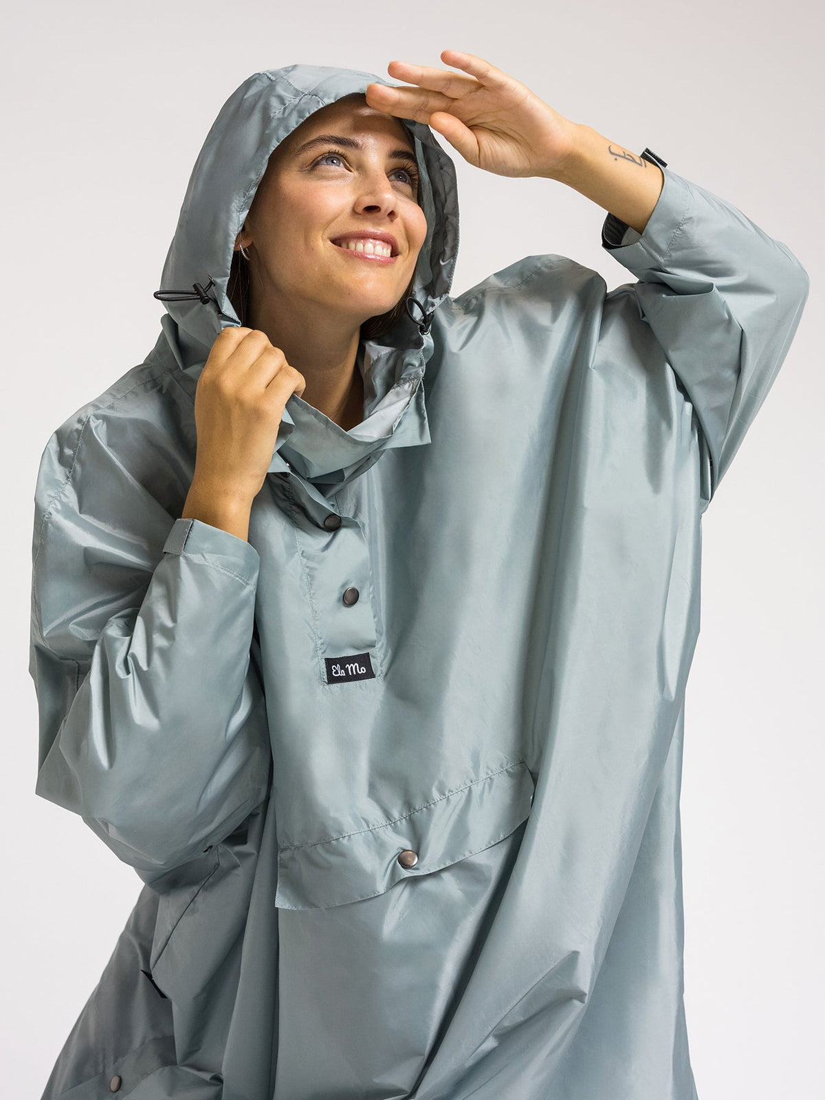 Ela Mo™ Regenponcho | Mint. Frau mit Regenponcho, hochgezogenem Kragen und Kapuze auf dem Kopf.
