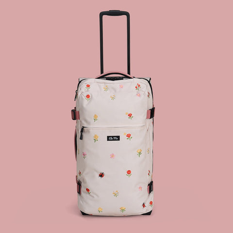 Ela Mo™ Reisetasche mit Rollen 78 Liter | Embroidery Edition Losy. Helle geblümte Tasche mit Tragegriff auf rosa Hintergrund.
