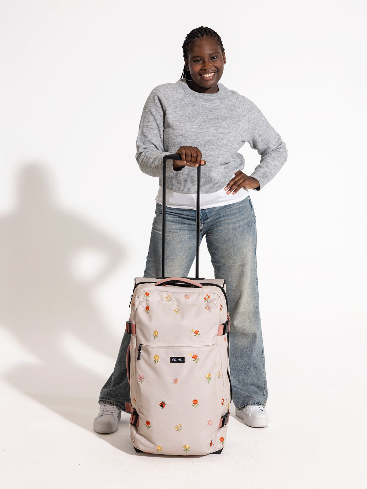 Ela Mo™ Reisetasche mit Rollen 78 Liter | Embroidery Edition Losy. Frau mit geblümter Reisetasche und hochgezogenem Griff.