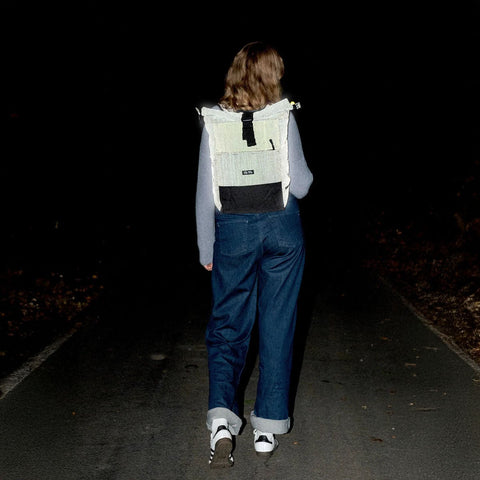 Ela Mo™ Rolltop Rucksack | Black Reflective. Eine Frau mit einem reflektierenden Rucksack in der Nacht.